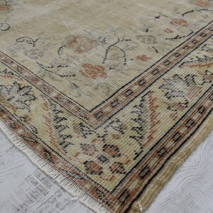May include: A vintage rug with a beige background and a floral pattern in shades of brown, black, and cream. The rug has a fringed edge and a border with a geometric design.