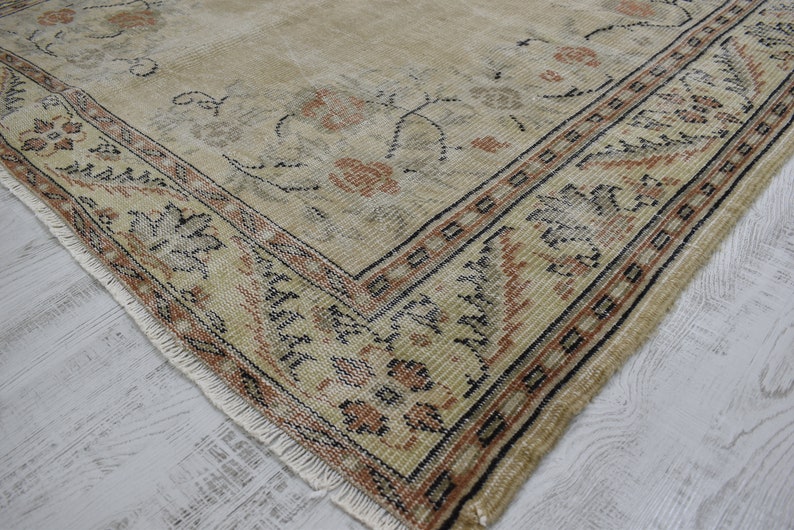 May include: A vintage rug with a beige background and a floral pattern in shades of brown, black, and cream. The rug has a fringed edge and a border with a geometric design.