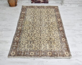 Puede incluir: Una alfombra vintage con fondo crema y un patrón floral marrón. La alfombra tiene un borde marrón con un diseño floral.