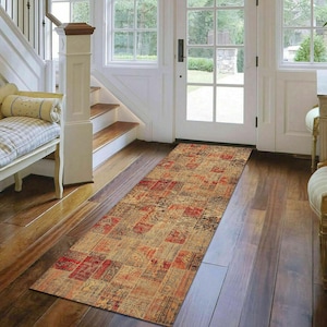 May include: A long, rectangular runner rug with a patchwork design in shades of red, brown, beige, and blue. The rug is laid out on a hardwood floor in a hallway.