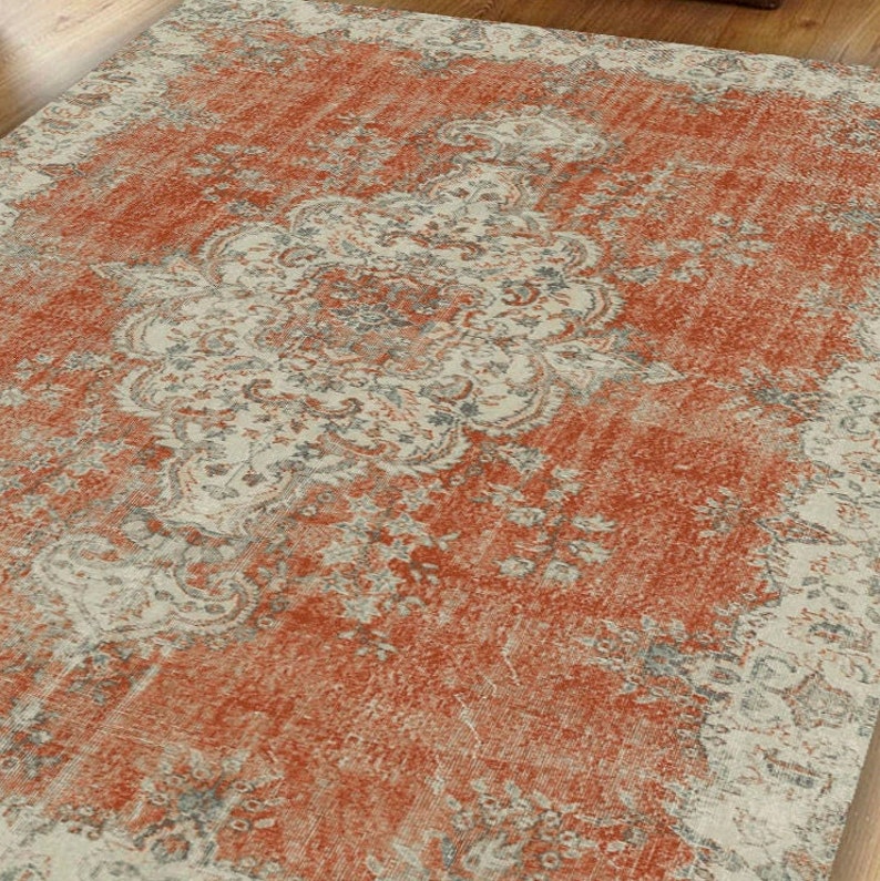 Puede incluir: Una alfombra de estilo vintage con un intrincado patr&oacute;n floral en tonos naranja, beige y gris. La alfombra tiene un aspecto desgastado y descolorido, lo que le da un aspecto r&uacute;stico y antiguo.