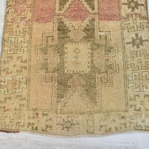 Puede incluir: Una alfombra turca vintage de corredor con fondo beige y intrincados patrones geom&eacute;tricos en tonos marrones y rosados. La alfombra tiene un borde con flecos y un aspecto desgastado y envejecido.