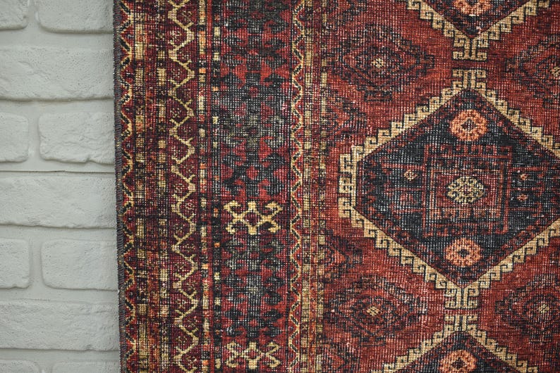 Op de afbeelding: Close-up van een gedeelte van een vintage tapijt met een complex geometrisch patroon. Het tapijt heeft een dieprode achtergrond met zwarte en gouden accenten. Diamant- en bloemmotieven zijn prominent aanwezig.