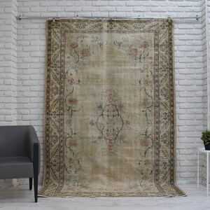 May include: A vintage rug with a beige background and a floral pattern in shades of brown, pink, and cream. The rug is hanging on a white brick wall.