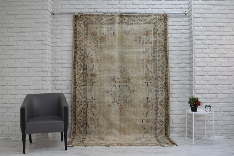 May include: A vintage rug with a beige background and a floral pattern in shades of brown, pink, and cream. The rug is hanging on a white brick wall.