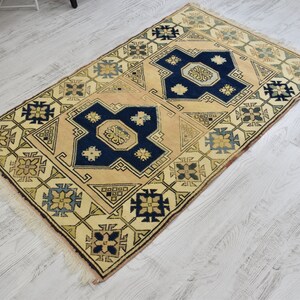 May include: A beige rug with a geometric pattern in shades of blue, yellow, and green. The rug has a fringe border.