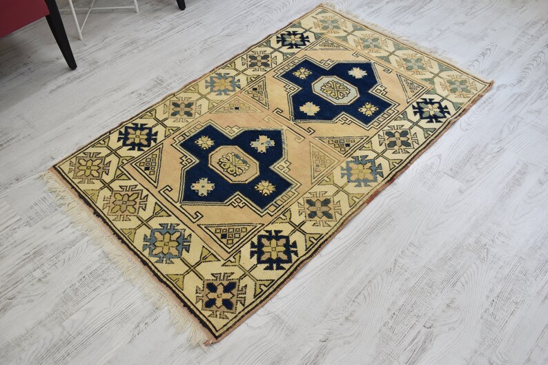 May include: A beige rug with a geometric pattern in shades of blue, yellow, and green. The rug has a fringe border.