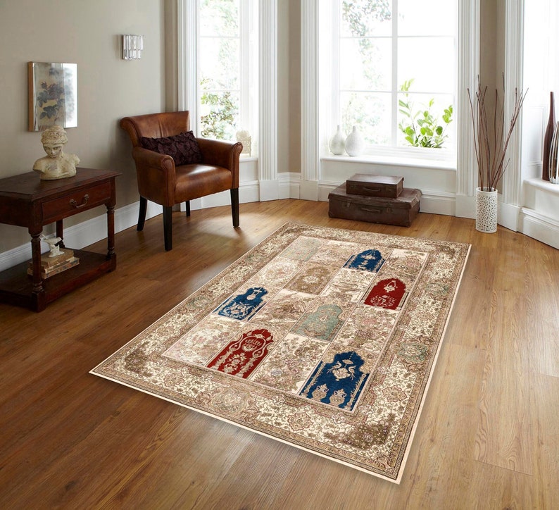 May include: A beige area rug with a patterned border and a patchwork design in the center. The rug features a variety of colors, including red, blue, and green. The rug is laid out on a hardwood floor in a living room setting.