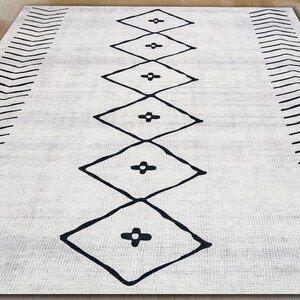 May include: A white rug with a black geometric pattern. The pattern features a series of diamonds with a plus sign in the center of each diamond.