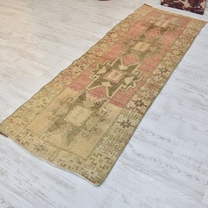 Puede incluir: Una alfombra de pasillo vintage con un esquema de color rosa p&aacute;lido y crema. La alfombra presenta un patr&oacute;n geom&eacute;trico con un dise&ntilde;o de estrella central.