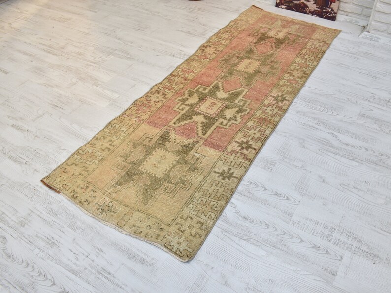 Puede incluir: Una alfombra de pasillo vintage con un esquema de color rosa p&aacute;lido y crema. La alfombra presenta un patr&oacute;n geom&eacute;trico con un dise&ntilde;o de estrella central.