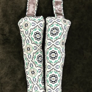 May include: Two white fabric doorstops with a green, black and blue geometric pattern. Each doorstop has a loop handle with a light brown satin ribbon.