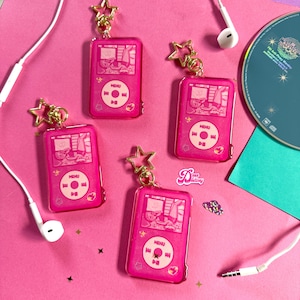 May include: Four pink acrylic keychain charms shaped like a retro music player, each with a gold star charm. The music player charms have a screen displaying a cartoon image and a circular control pad. Earbuds and a CD are also in the image.