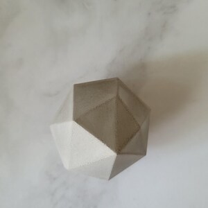 May include: A geometric concrete sculpture with a light grey colour and a smooth, slightly textured surface.