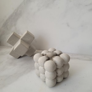 Peut inclure: Deux sculptures en béton, l'une en forme de croix et l'autre en forme de cube avec une surface texturée. Le cube est composé de nombreuses petites sphères.