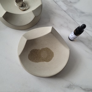 May include: Two small, light gray ceramic dishes. One dish has a ring inside. The other dish has a brown stain in the center.