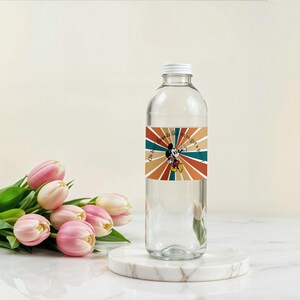 May include: A clear glass water bottle with a white cap and a colorful label featuring Mickey Mouse. The label has a retro design with orange, teal, and brown stripes radiating from Mickey. The text on the label reads "Oh boy, I've got a plan."