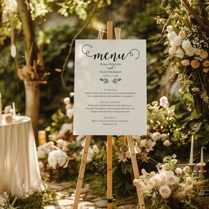 May include: A white wedding menu sign on a wooden easel. The menu includes the names Rima Horton and Alan Rickman, and the date August 17, 2006. The menu lists a starter, main course, and dessert.