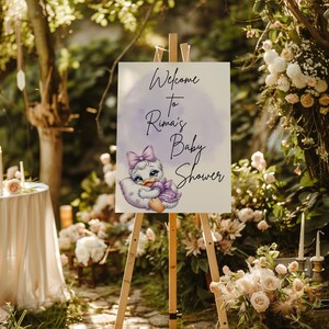 May include: Welcome to Rima's Baby Shower sign with a purple watercolor background and a cartoon duckling wearing a purple dress and a bow.