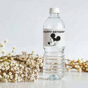 May include: A clear plastic water bottle with a white cap. The label reads "HAPPY BIRTHDAY" and features a black and white image of Mickey Mouse. White flowers are in the background.