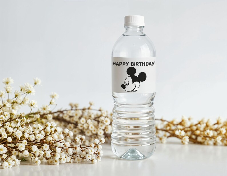 May include: A clear plastic water bottle with a white cap. The label reads "HAPPY BIRTHDAY" and features a black and white image of Mickey Mouse. White flowers are in the background.