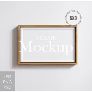 May include: A rectangular wooden frame with a white interior, displaying the text "FRAME Mockup." The frame has a light brown colour and is set against a white background. The image also includes the text "5X3" and "JPG PNG PSD."