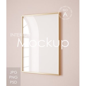 Puede incluir: Una maqueta de marco de imagen dorado en una pared de color rosa claro. El marco está vacío y listo para tu diseño.