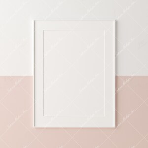 Puede incluir: Un marco de fotos blanco con un paspart&uacute; blanco, colocado contra una pared de dos tonos. La mitad superior es blanca y la mitad inferior es de un rosa suave. El marco est&aacute; vac&iacute;o, listo para una obra de arte o una fotograf&iacute;a.