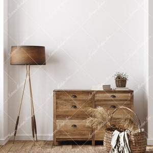 May include: A wooden dresser with six drawers, a brown lamp with a tripod stand, a woven basket with a white cloth, and a small potted plant with white flowers. The dresser and basket are on a light brown rug in front of a white wall.