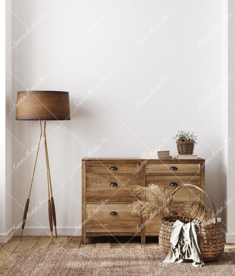 May include: A wooden dresser with six drawers, a brown lamp with a tripod stand, a woven basket with a white cloth, and a small potted plant with white flowers. The dresser and basket are on a light brown rug in front of a white wall.
