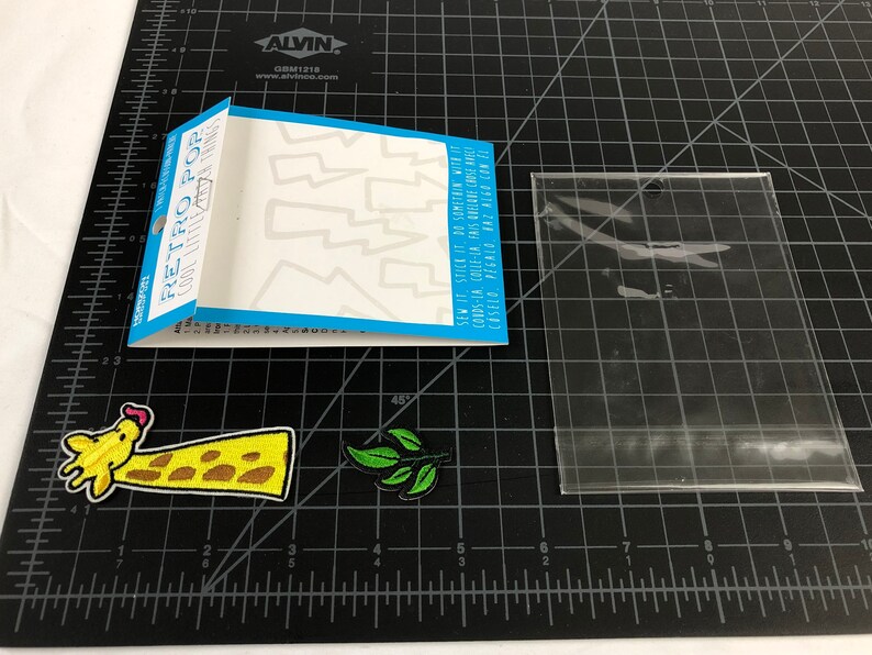 以下が含まれることがあります： 稲妻のデザインのアイロン接着パッチのシート。シートには「レトロポップクールリトルシングス」とラベルが貼られています。また、キリン、緑の葉、透明なビニール袋のアイロン接着パッチが3つあります。