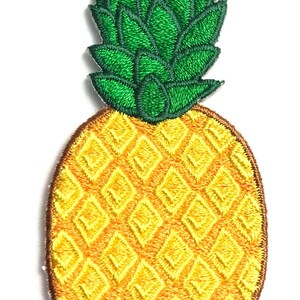 May include: An embroidered patch shaped like a pineapple. The fruit body is yellow with a brown diamond-patterned outline, and the leafy top is composed of multiple pointed green segments with dark green thread detailing throughout the design.