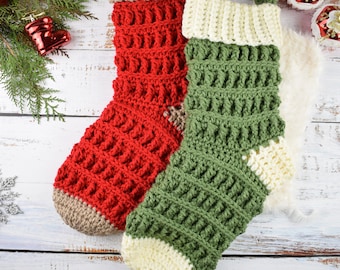 May include: Two crocheted Christmas stockings, one red and one green, with white and brown accents. The stockings are hanging on a white wooden background.
