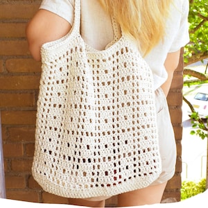 May include: A white crocheted tote bag with a large open weave pattern. The bag is being worn by a person, but the person's face is not visible.