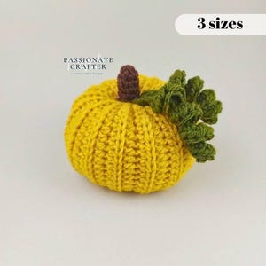 May include: A yellow crocheted pumpkin with a brown stem and curly green leaves. The text "PASSIONATE CRAFTER" and "3 sizes" are visible in the image. The pumpkin features a ribbed texture created by the crochet stitches throughout the body.