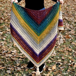 May include: A colourful crocheted shawl with a striped pattern in shades of burgundy, purple, grey, beige, yellow, green, and teal. The shawl has fringe tassels on the ends.