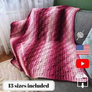May include: A handmade, textured crochet blanket in shades of pink and red, draped over a gray armchair. The blanket features a vertical striped pattern with a raised, leaf-like design. The text "13 sizes included" is visible.