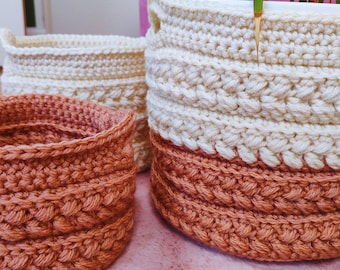Puede incluir: Tres cestas de ganchillo hechas a mano en varios tamaños y colores. La cesta más grande es de color blanquecino con una base de color terracota. La cesta mediana es de color blanquecino. La cesta más pequeña es de color terracota. Las cestas están diseñadas para guardar cosas o como macetas decorativas.