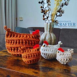 May include: Crocheted chicken-shaped baskets in various sizes, with red comb details. The baskets are in shades of brown and beige, arranged on a wooden surface. A vase with dried flowers is in the background. The text "PASSIONATE CRAFTER" is visible.