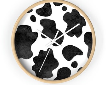May include: A round wooden wall clock with black and white cow print design. The clock hands are white.