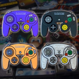 May include: Four enamel pins of the Nintendo GameCube controller in different colors: purple, gray, orange, and silver.