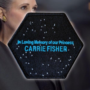 May include: A black hexagonal patch with white stars and the text "In Loving Memory of our Princess CARRIE FISHER" in blue.