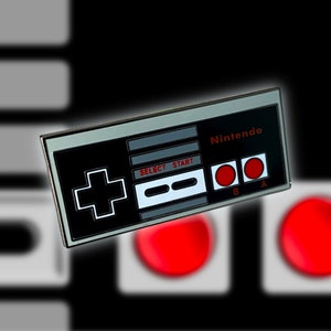 May include: A silver and black Nintendo controller pin with red buttons. The pin features the words "Nintendo" and "Select" and "Start" on the controller.