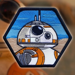 May include: A hexagonal embroidered patch featuring a white and orange droid with a blue and white background. The droid has a large, round head with a black eye and a small, round mouth.