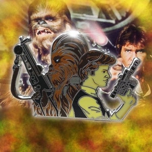 May include: A Star Wars-themed pin featuring Chewbacca, Han Solo, and a blaster. The pin has a silver outline with detailed character designs and a yellow and brown color scheme. The background includes images of the characters.