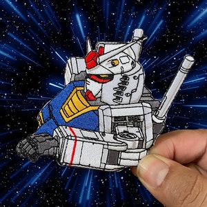 May include: A white, blue, and red embroidered patch of a robot with a large gun. The robot is in a flying pose with its legs extended. The patch is set against a black and blue starry background.