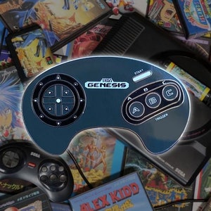 May include: A gray Sega Genesis controller pin with a black directional pad, three black buttons labeled A, B, and C, and a black trigger button labeled "TRIGGER". The pin has the text "SEGA GENESIS" in white letters.
