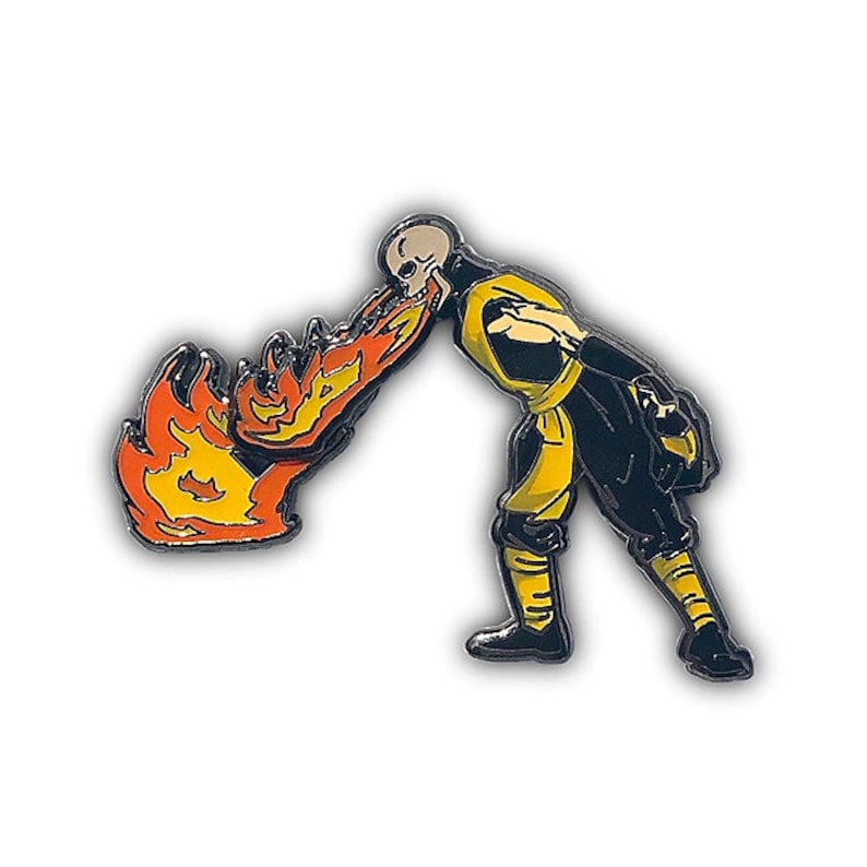 May include: A black and yellow enamel pin of a character from the video game Mortal Kombat. The character is breathing fire, which is depicted in orange and yellow enamel.