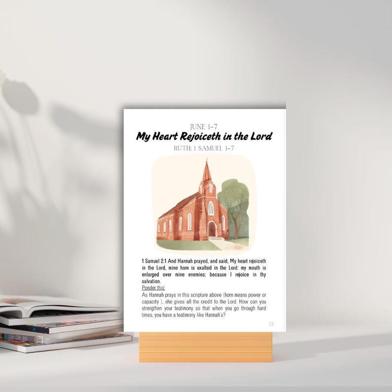 Op de afbeelding: Een bedrukte kaart met de tekst "My Heart Rejoiceth in the Lord" en een aquarel illustratie van een kerk. De kaart wordt gepresenteerd op een houten standaard. De tekst bevat de bijbelverwijzing "RUTIE I SAMUEL 1-7".
