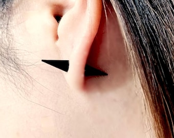 May include: A pair of black triangle shaped earrings worn in the earlobe of a person with dark hair.